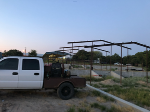 White pickup truck next to unfinished structures with metal frames. Dusk setting.