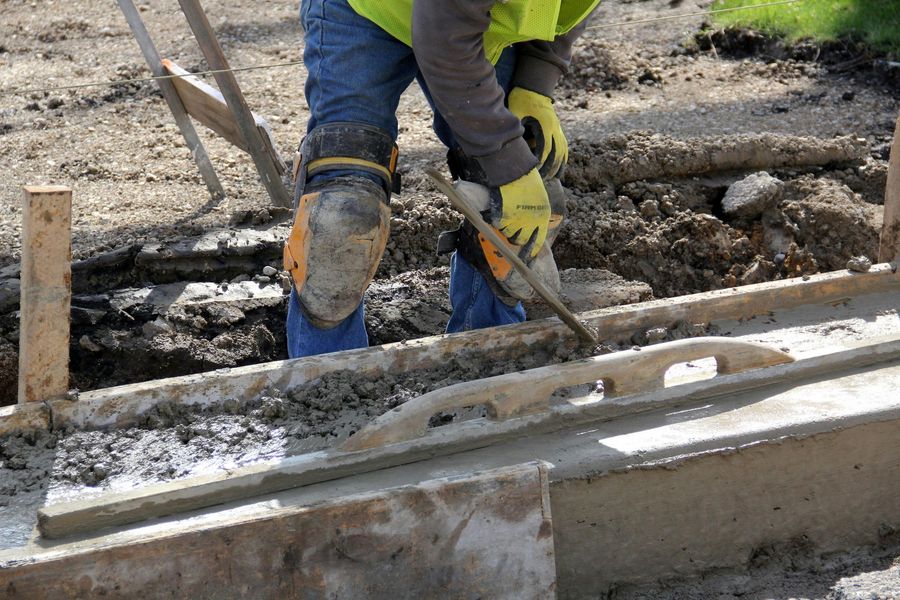 Person using a tool to smooth wet concrete in a construction site.