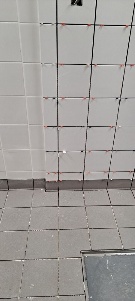 Tiled wall and floor; some tiles are being installed with spacers; a small electrical box is visible.