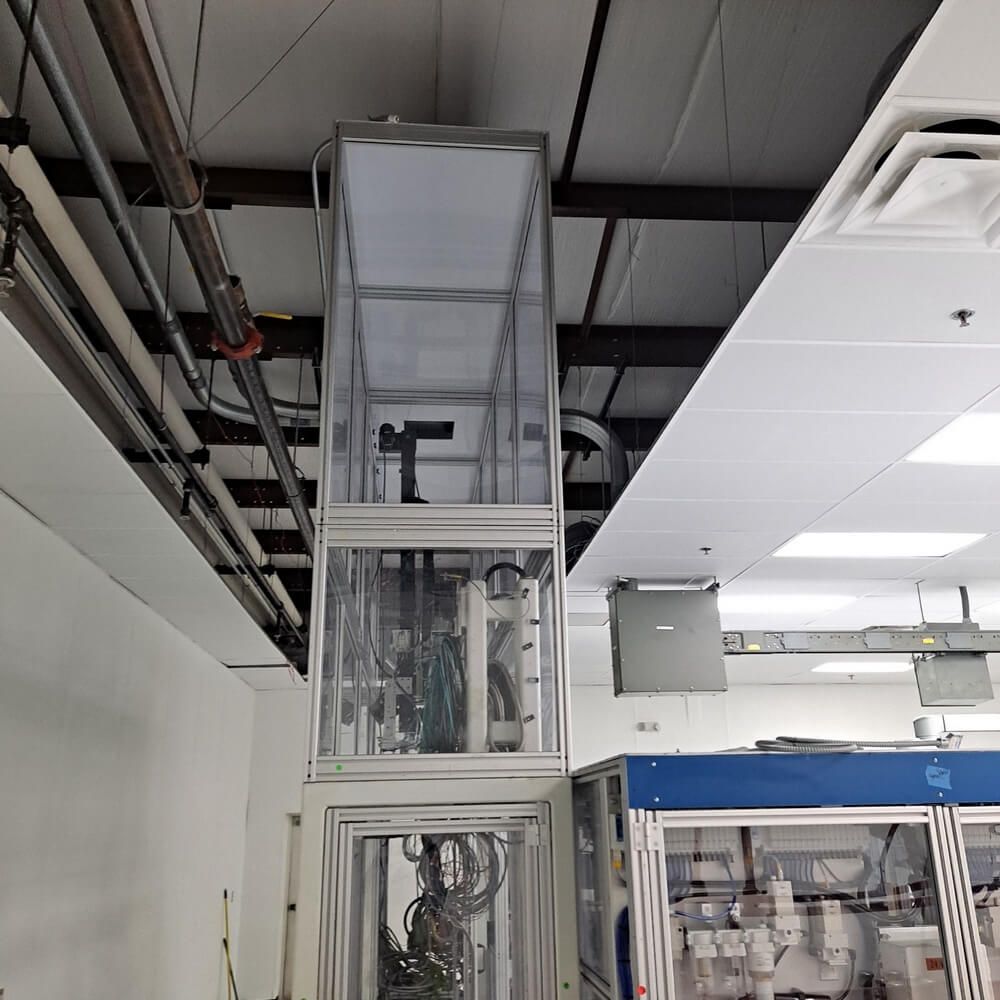 An industrial robot encased in a transparent tower in a laboratory setting.