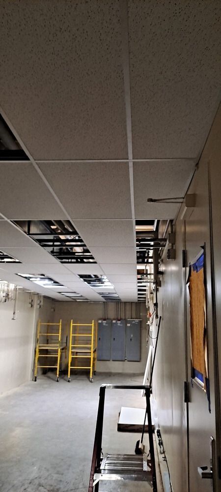 A room with a partially installed ceiling. Two yellow ladders sit in the empty space.