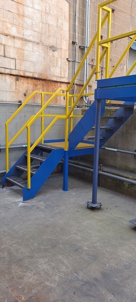 Blue and yellow metal stairs with handrails against a concrete wall.