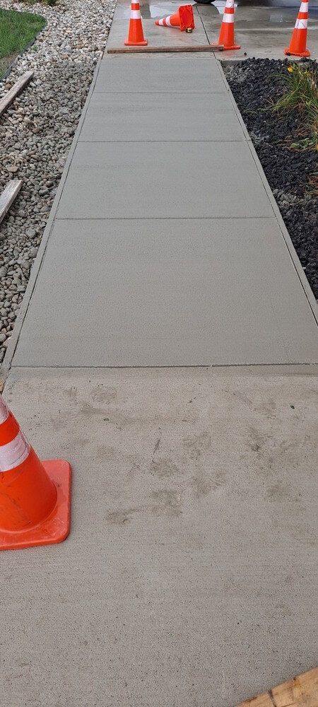 Freshly poured concrete sidewalk, orange cones for caution.