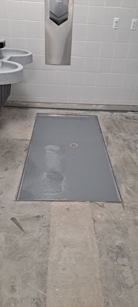 A restroom with a large, rectangular floor drain in front of the hand dryer and sinks.