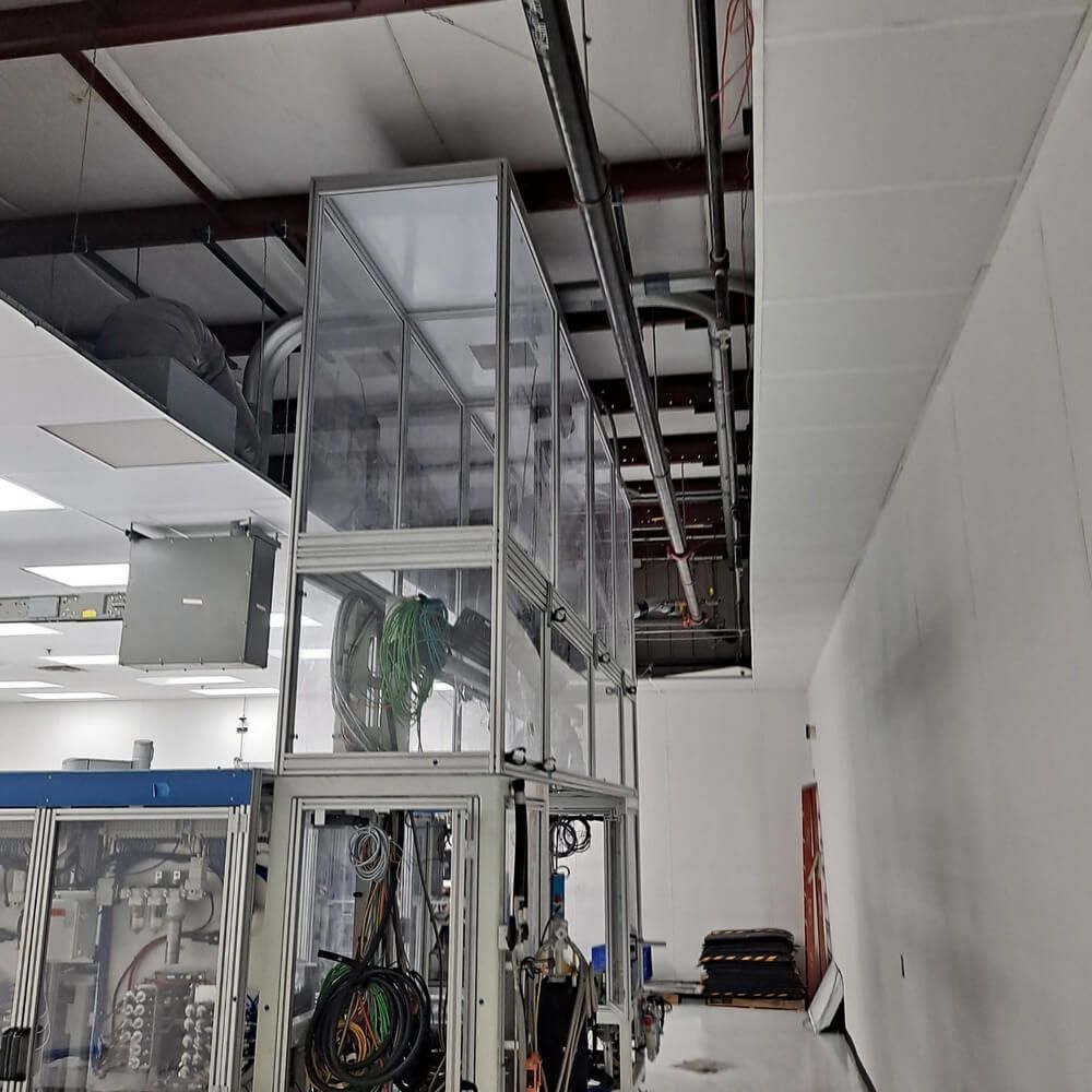 Clear plastic machinery enclosures in a factory setting, with exposed wiring and overhead infrastructure.