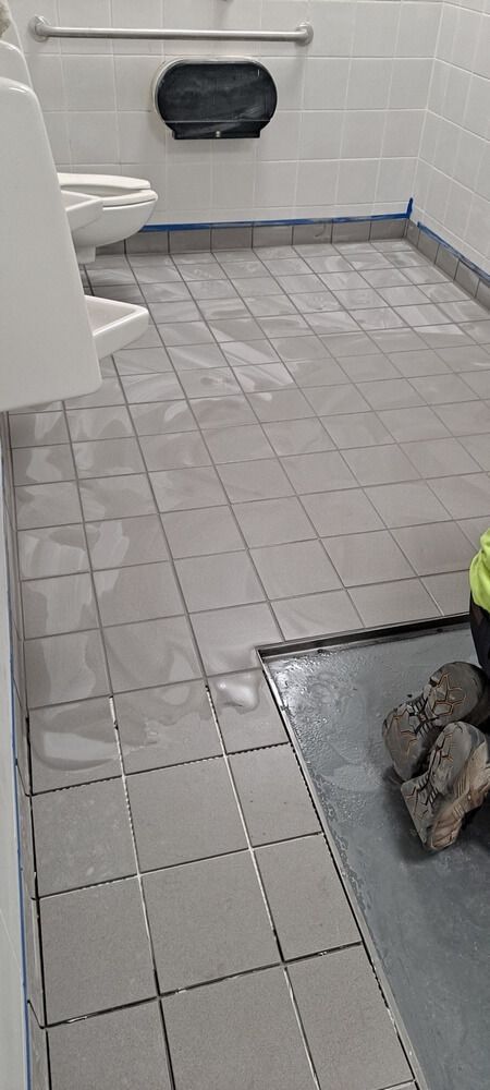 A public restroom with gray tiled floor and a urinal on the left.