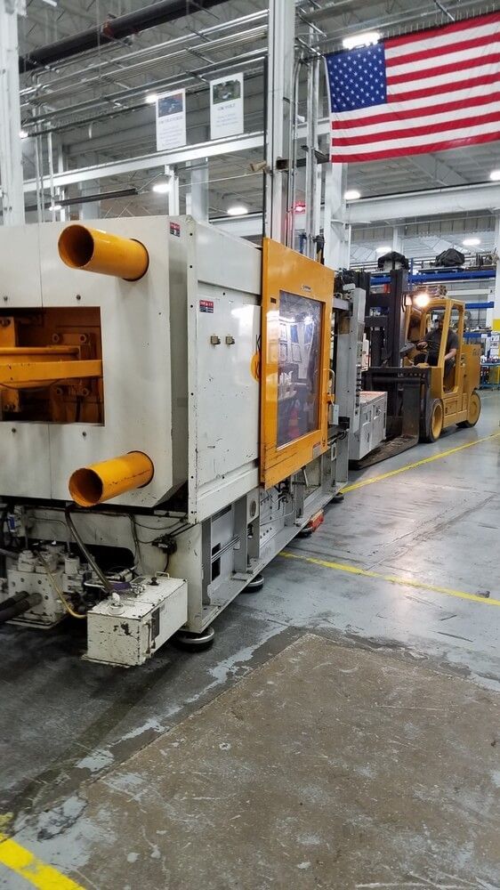 Industrial machine with a forklift in a factory setting, American flag in background.