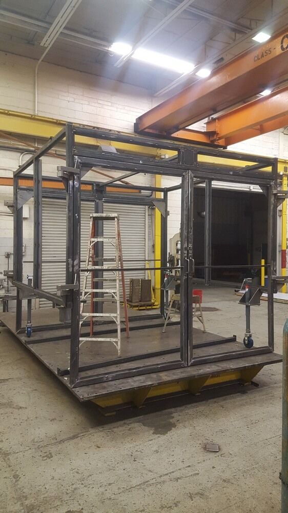 Steel cage structure on a platform in a workshop; ladder inside.