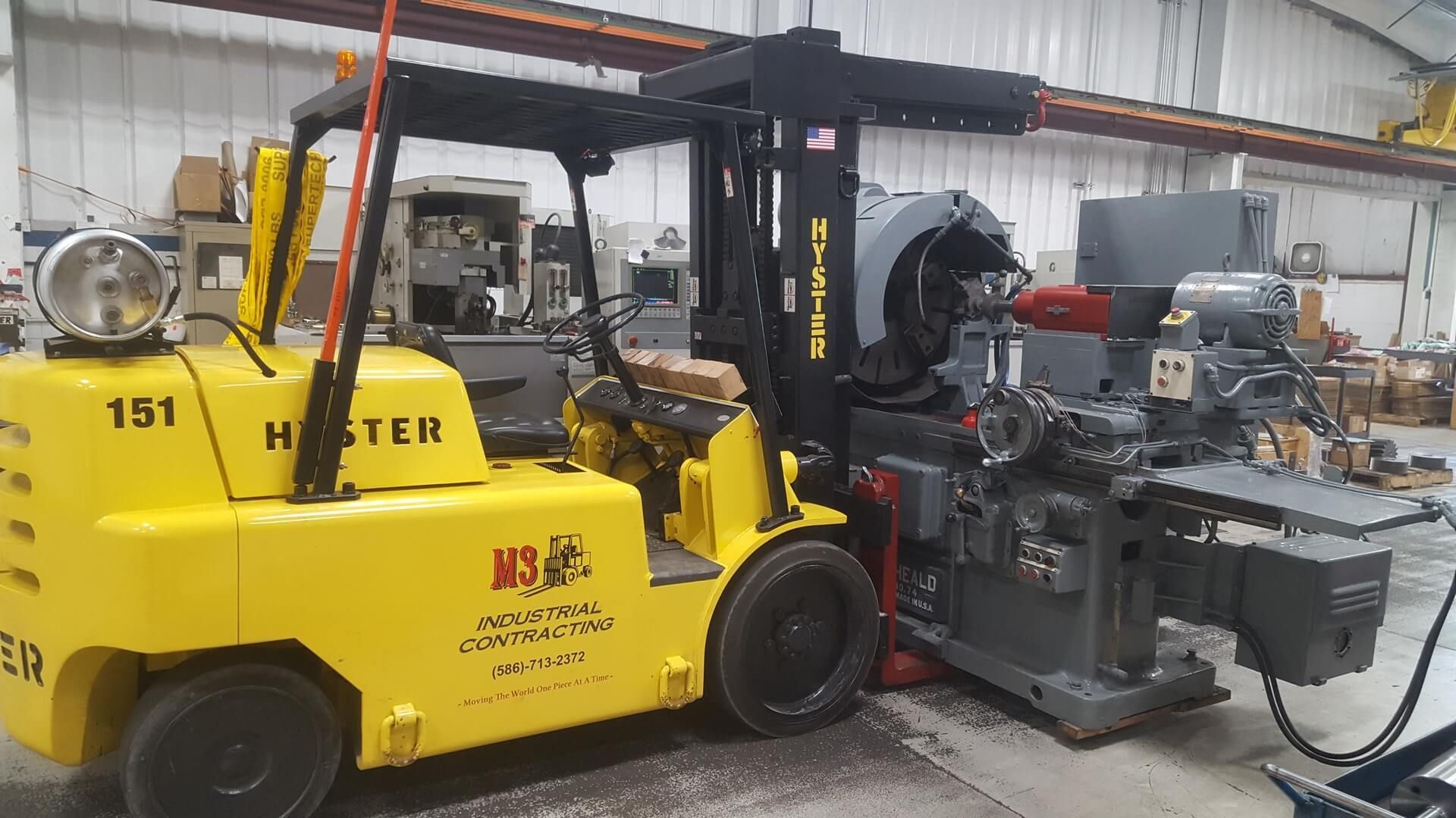 A yellow forklift is lifting a machine in a factory.