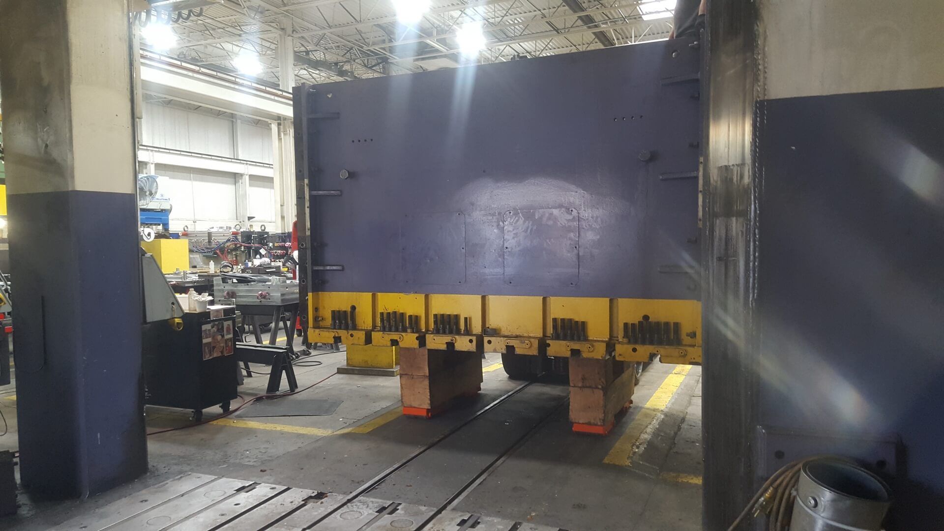 Large industrial press machine, blue and yellow, in a factory setting.