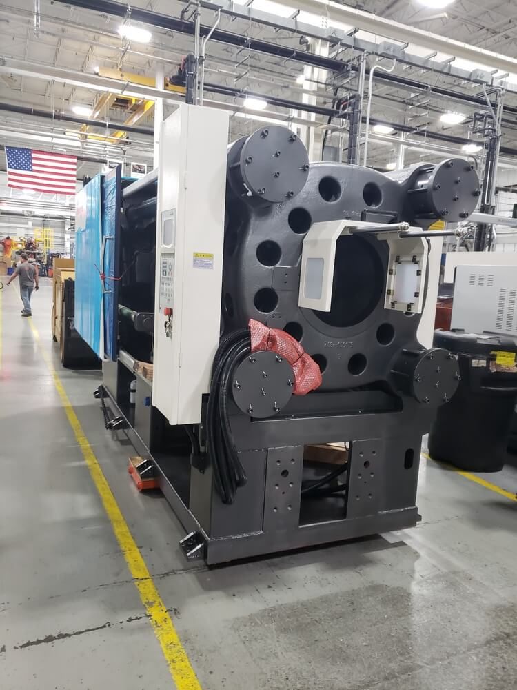 Large, industrial injection molding machine in a factory setting with a US flag.