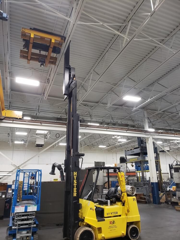 Yellow forklift lifting a large metal object near the ceiling of a factory.