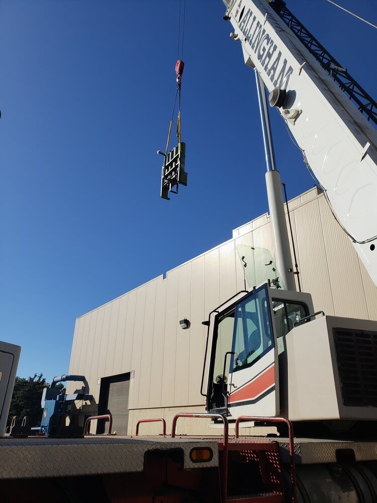 A crane lifting equipment near a beige building on a sunny day.
