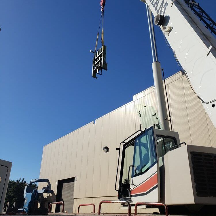 Crane lifting a metal structure near a building on a sunny day.