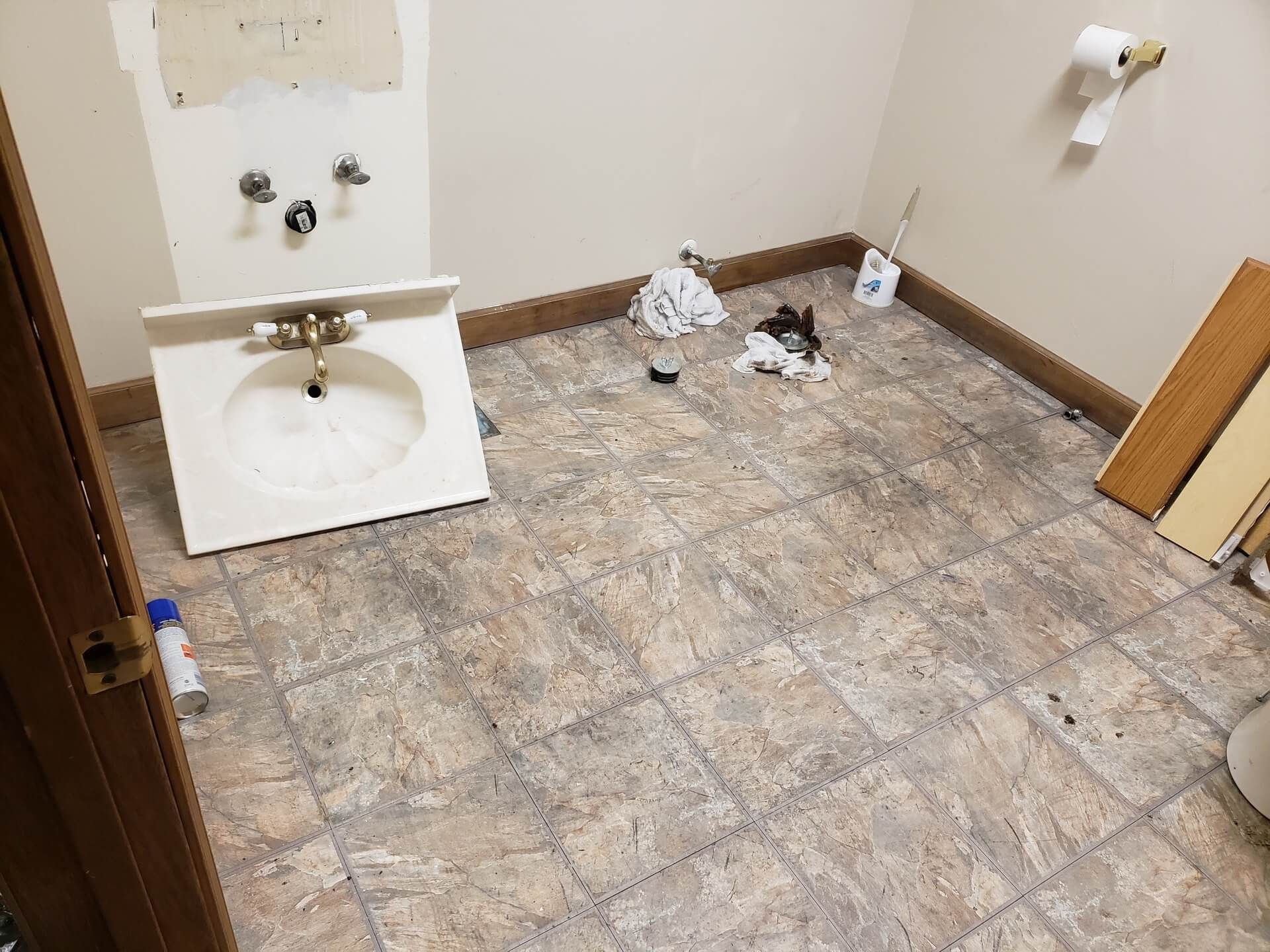 Bathroom renovation in progress, sink removed. Beige walls and floor with scattered debris.