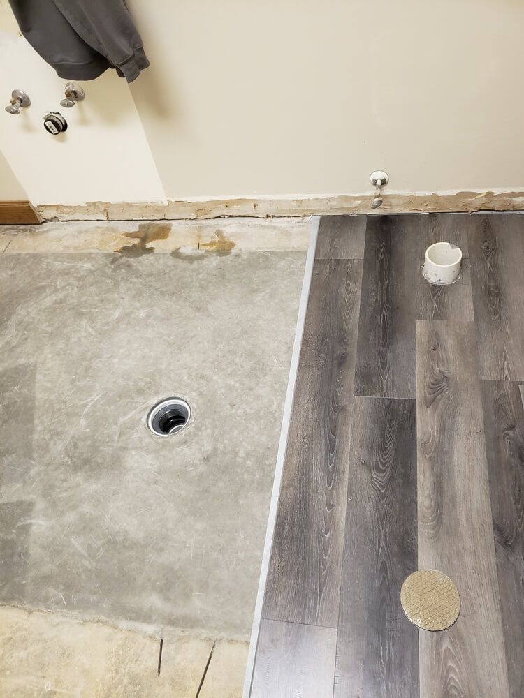 Bathroom undergoing renovation with new vinyl plank flooring installed next to the exposed concrete subfloor.