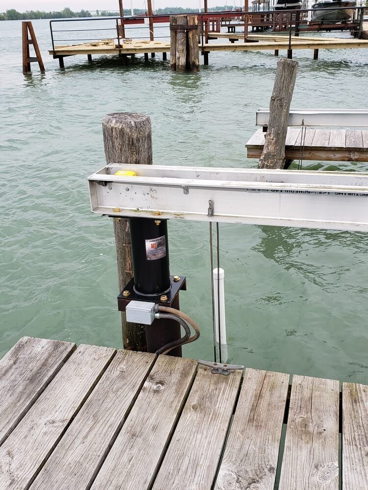 Boat lift on a wooden dock at a lake. Motor, support beam, and guide pole. Green water.
