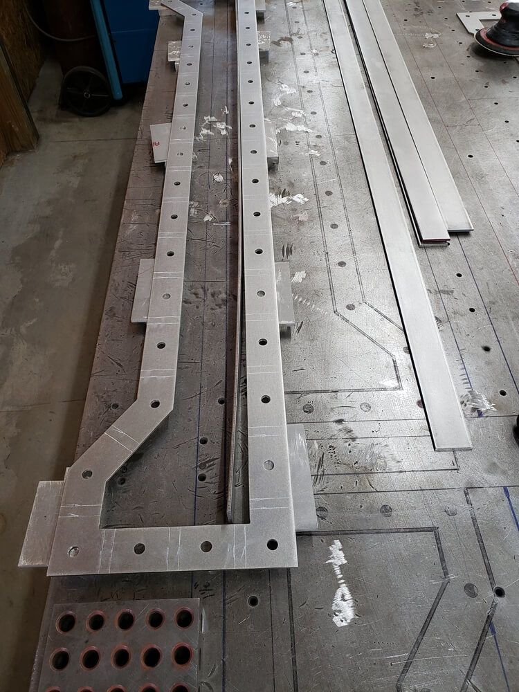 Metal parts with holes and markings laid out on a steel table.
