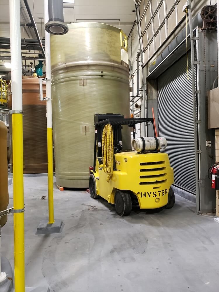 Yellow forklift in a warehouse near a large cylindrical tank wrapped in plastic.