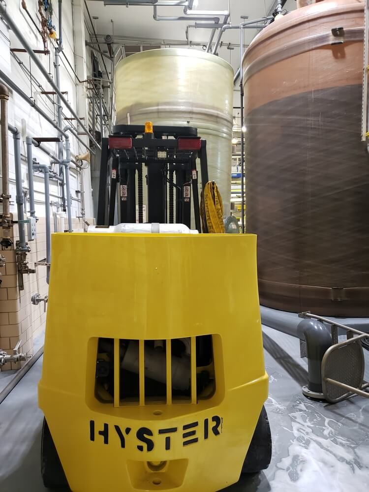 Yellow Hyster forklift in industrial setting, with large tanks and pipes.
