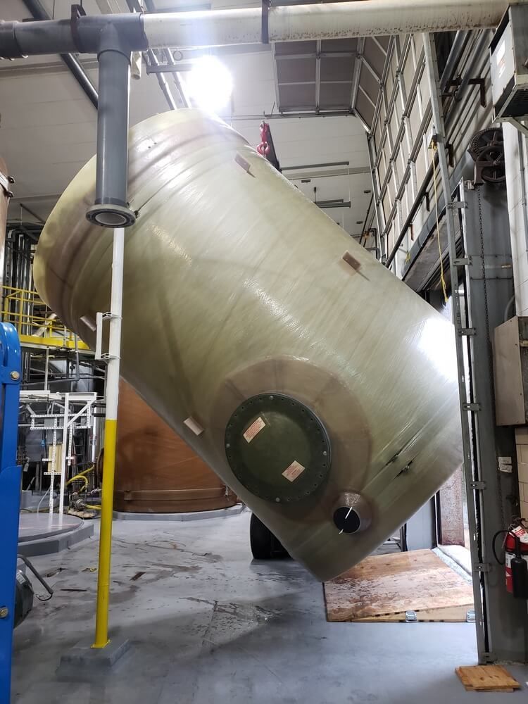 Large cylindrical tank in a factory, tilted and held by support beams.