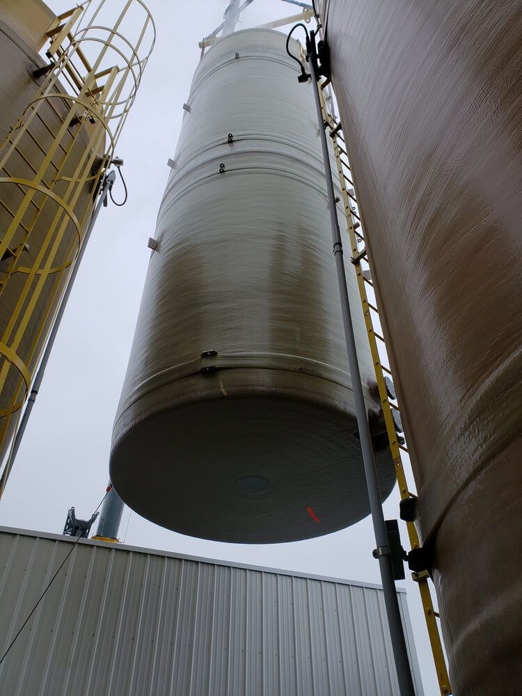 Large cylindrical tank being lifted between two other tanks. A ladder is visible.