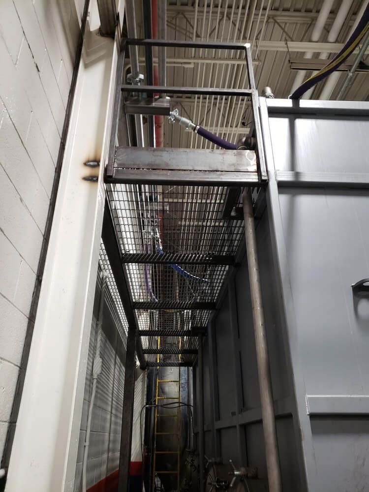 Metal platform with steps attached to a tall industrial structure.