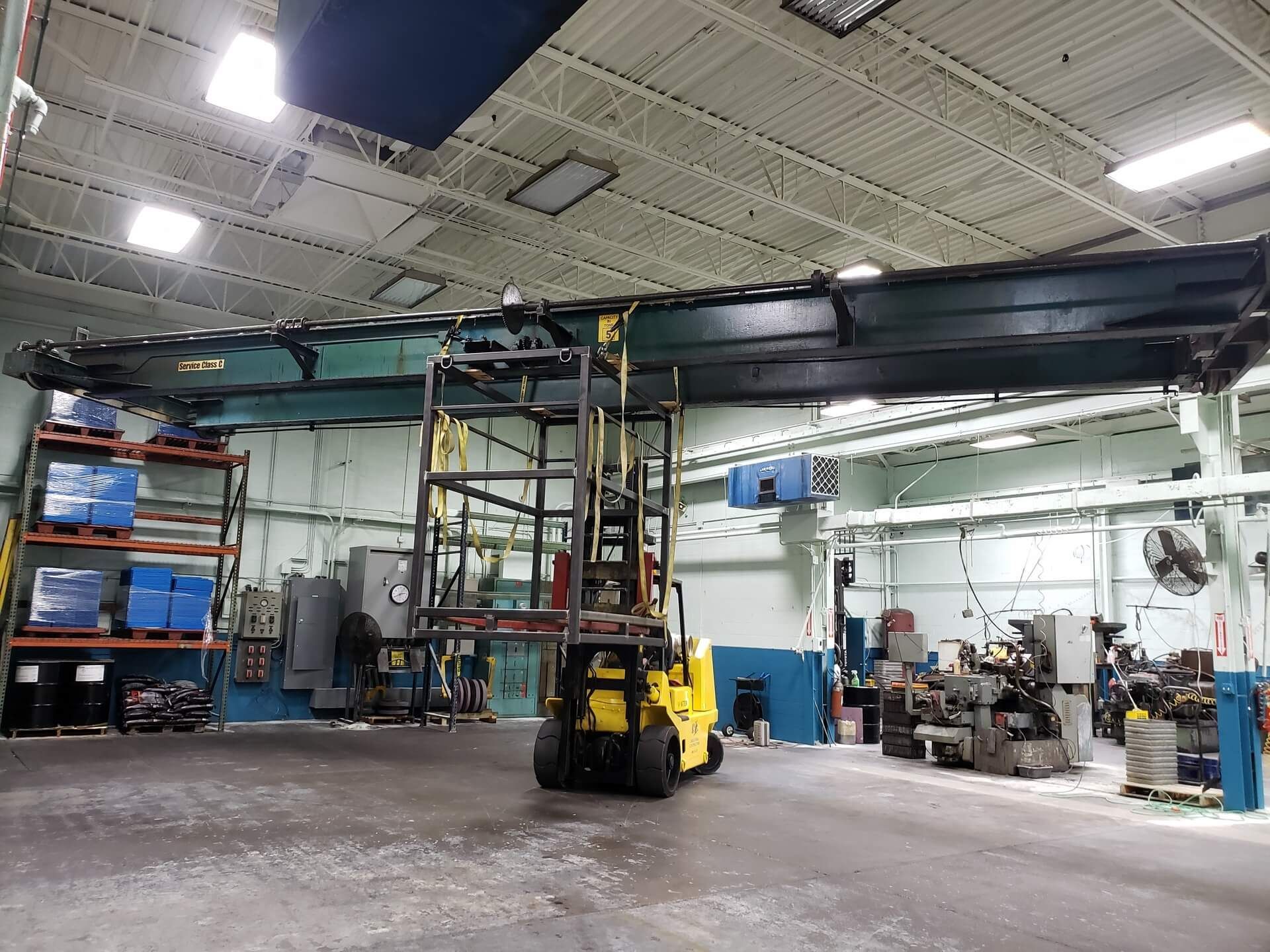 Forklift beneath a large overhead crane in a factory setting.