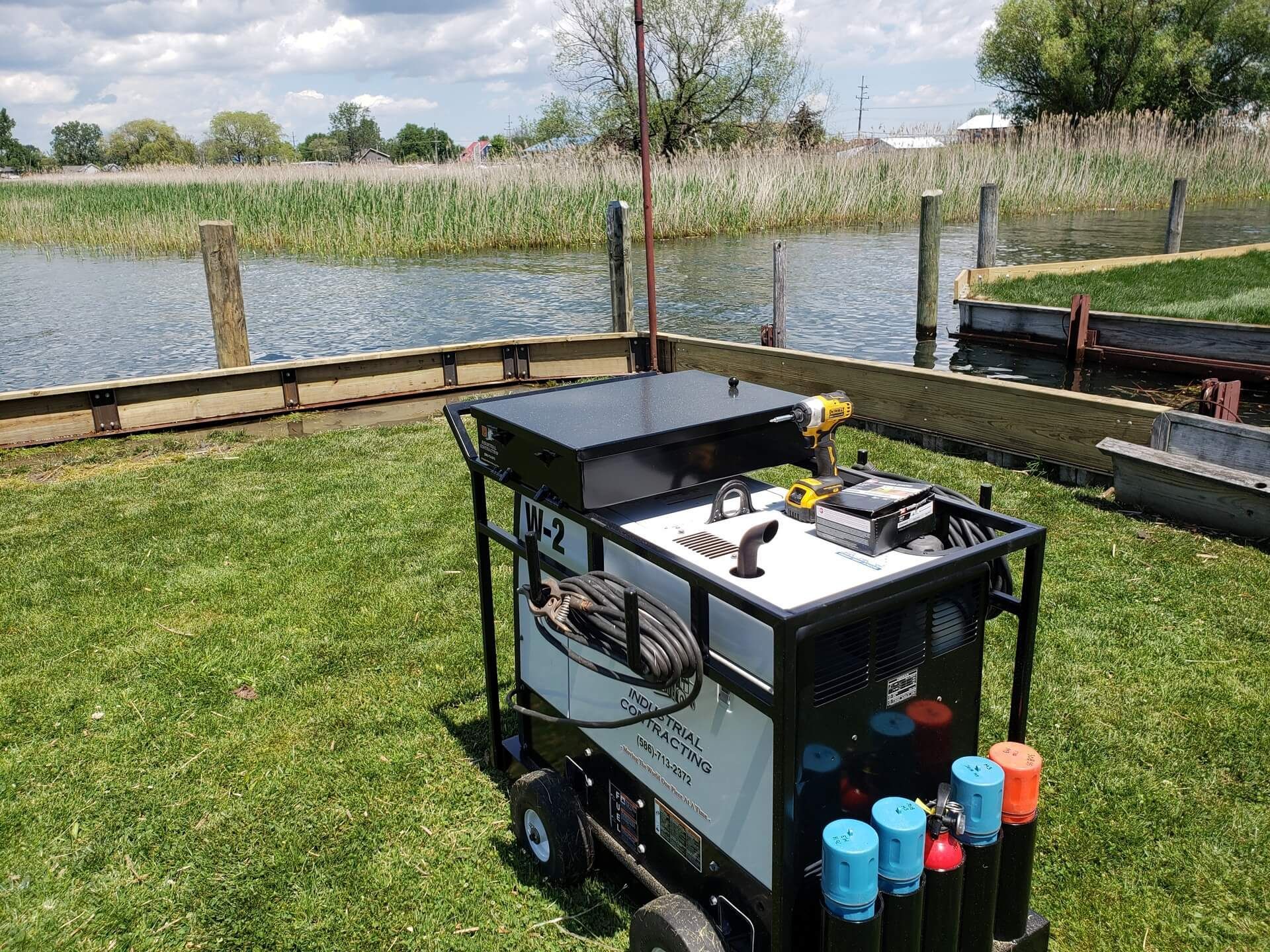 Welding machine on wheels near a lake, grassy area.