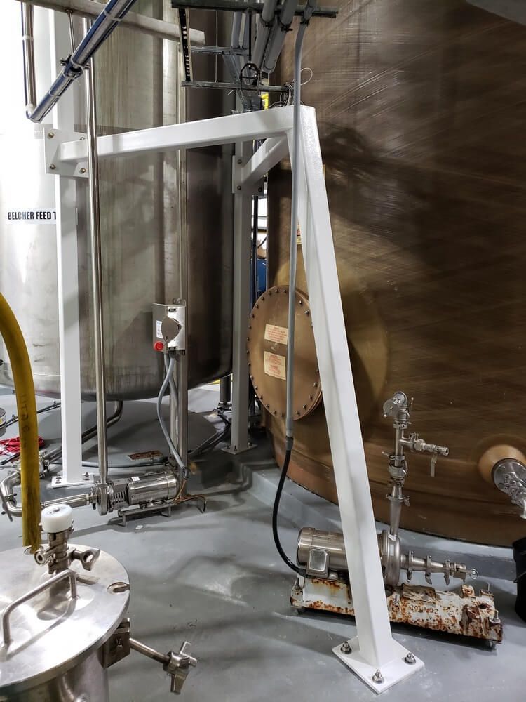 White metal industrial equipment next to a large stainless steel tank and a smaller beige tank in a factory.