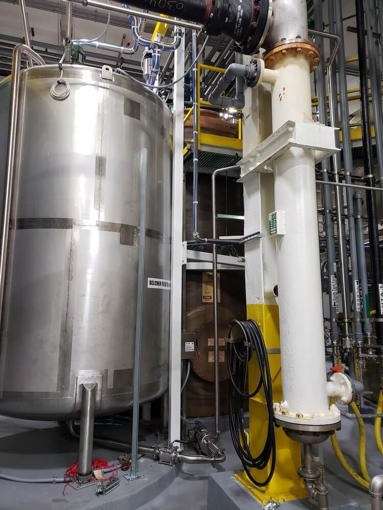Stainless steel industrial tank and vertical structure with piping in a factory setting.