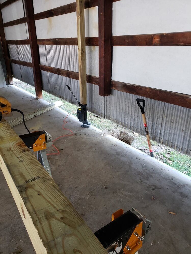 Construction site: wooden post being installed, concrete floor, power saw, shovel, and lumber present.