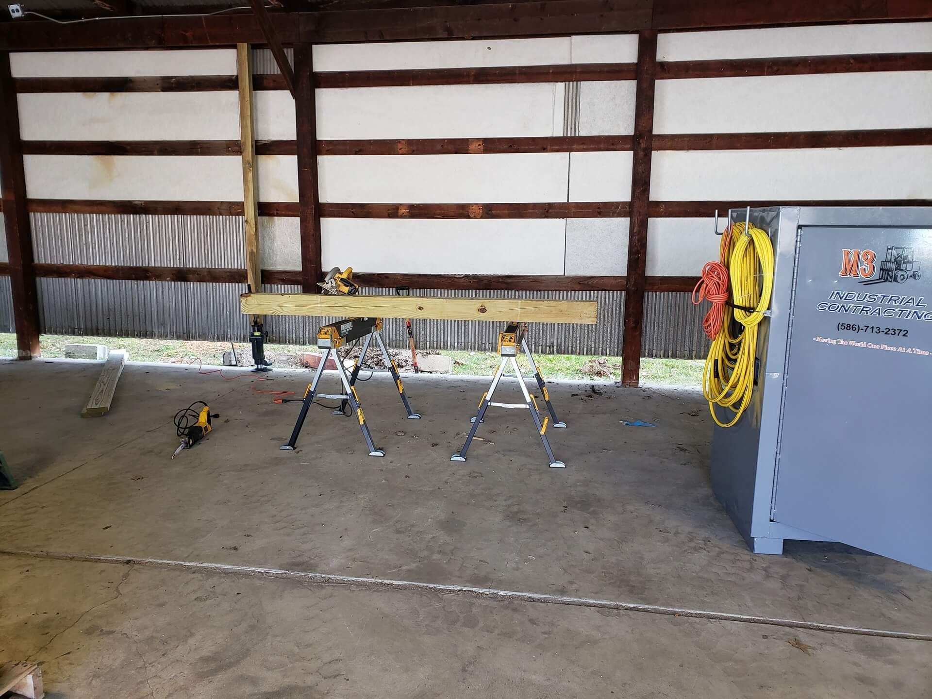Sawhorses support a wooden beam in a barn, tools nearby.