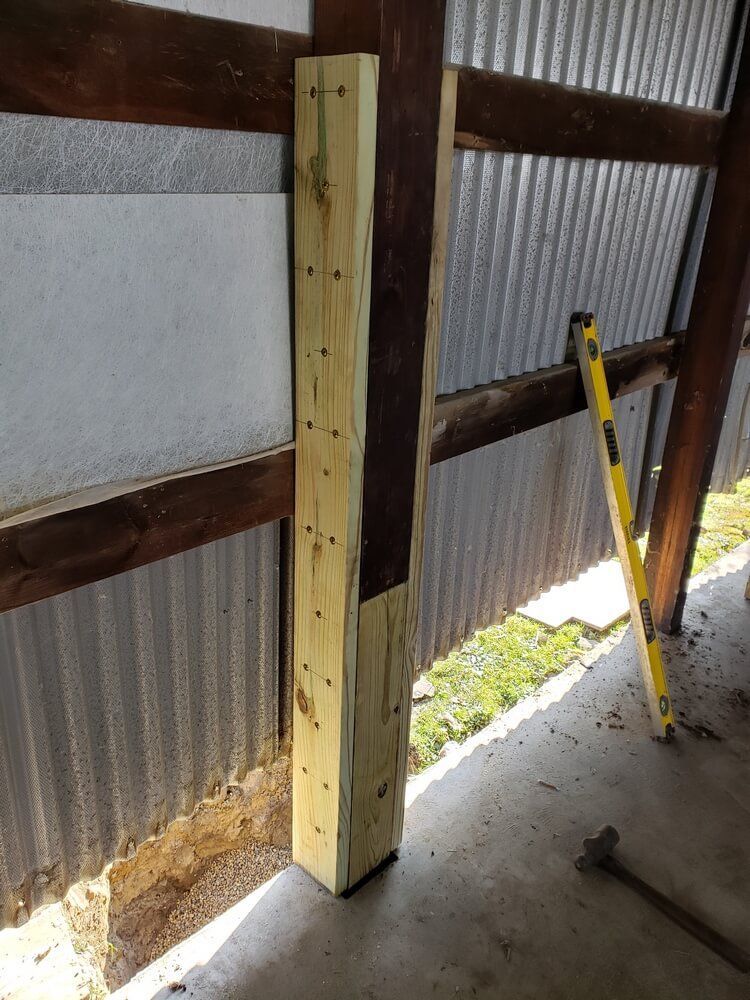 A wooden post secured to a corrugated metal wall, with a level leaning against it.