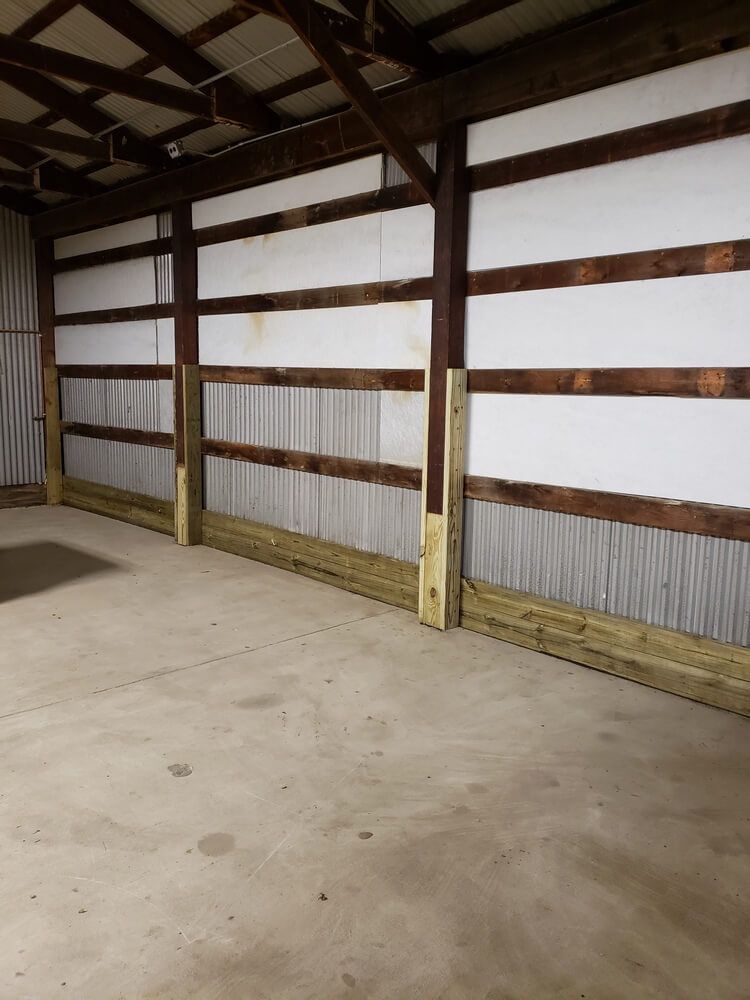 Interior view of a building with wooden beams and metal siding, concrete floor, and white insulation panels.