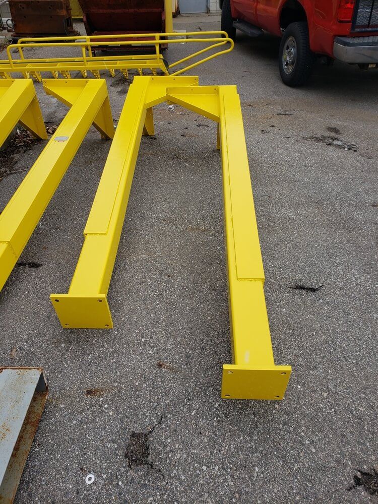 Yellow steel support beams, bolted to concrete, next to a red truck.