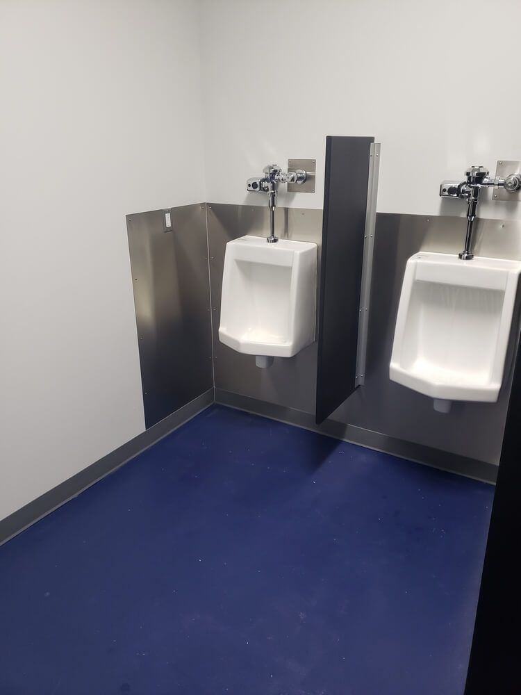 Two white urinals with metal dividers, blue floor, white walls.