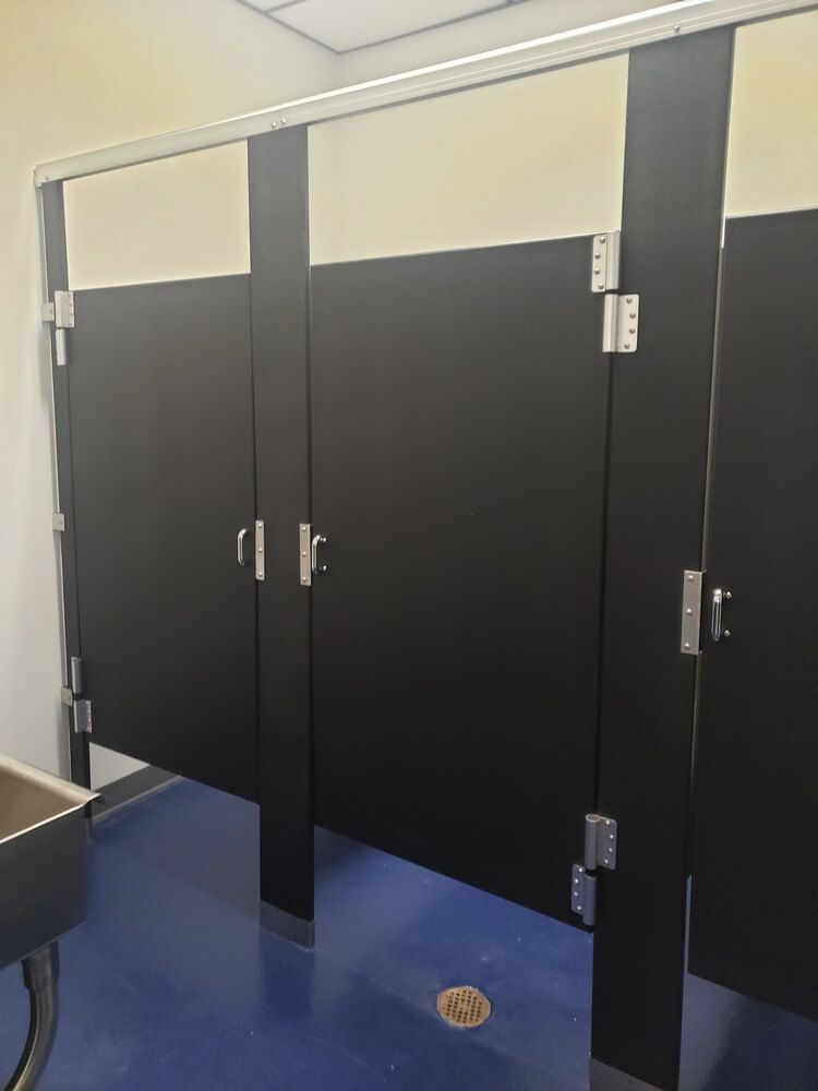 Public restroom stalls, black doors, silver hardware, cream-colored tops, blue floor.