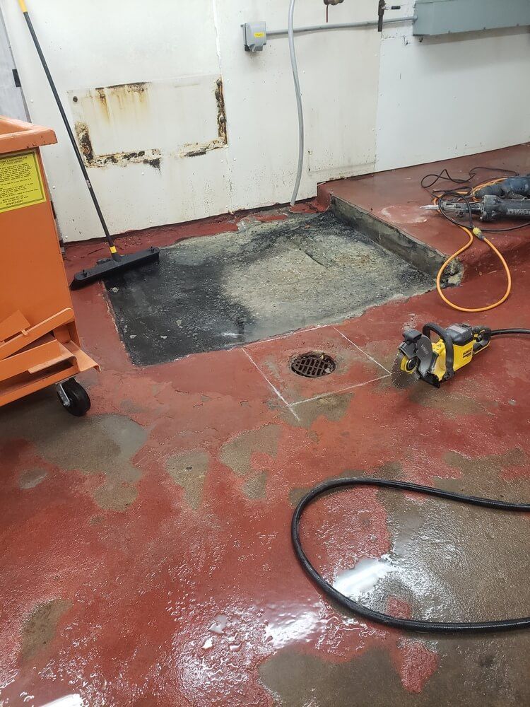 Red floor with cut-out section. A power saw and a hose lie nearby.  A cart and broom are also in the room.