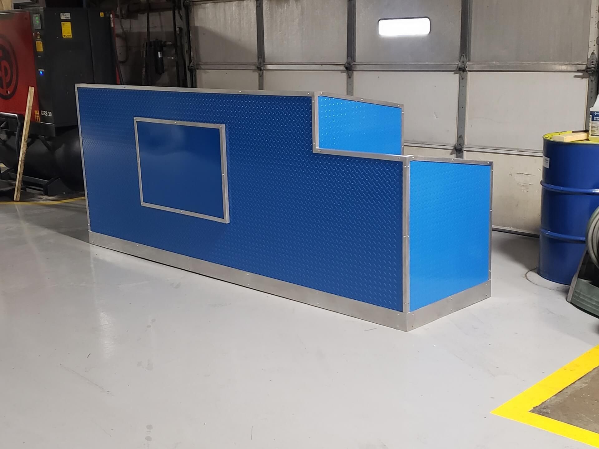Blue diamond-plate counter with a cutout window and metal trim in a workshop.