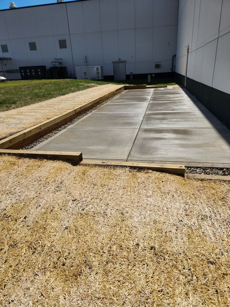 Concrete pad bordered by wood and gravel, adjacent to a building.