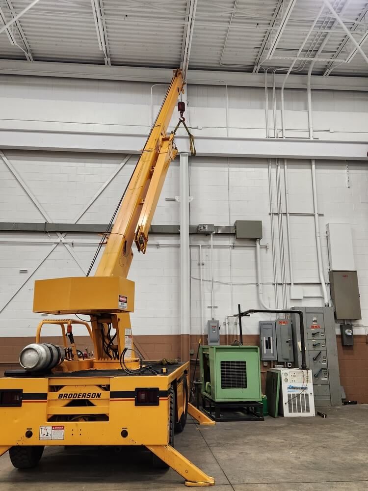 Yellow industrial crane inside a warehouse. Crane arm is extended upwards.