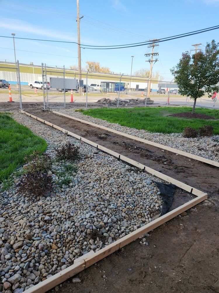 Pathway under construction with wooden borders and gravel. Grassy area with fence in background.