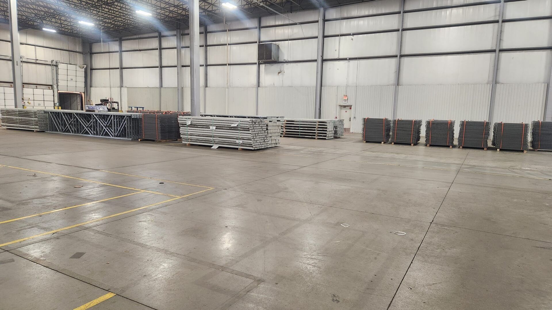 Large industrial warehouse interior with stacks of metal beams on the floor.