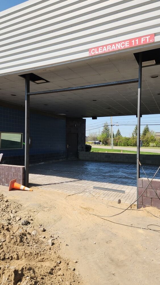Drive-thru entrance with 11 ft clearance. Metal frame supports awning. Ground level dirt and construction cone present.