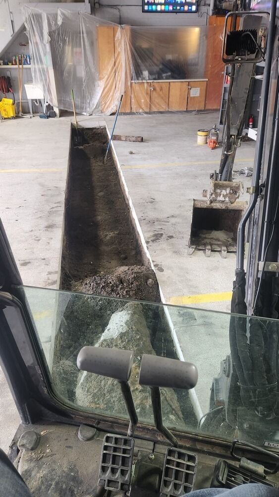 Inside a backhoe, view of its scoop filled with dirt in a construction setting. Another backhoe is in the background.