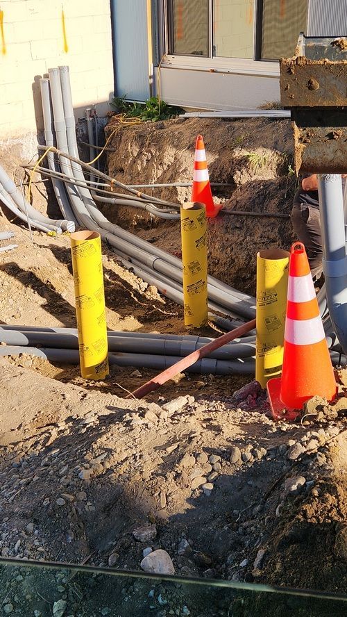 Construction site with buried pipes, yellow safety posts, and orange cones.