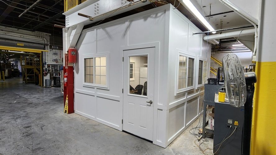 White office cubicle with windows and door in a factory setting.
