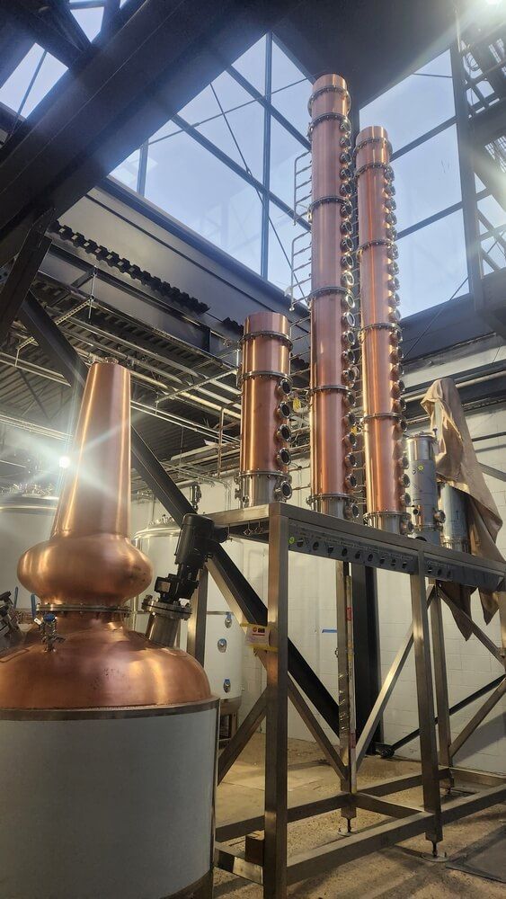 Copper stills inside a distillery, with tall columns and a conical top, set against a metal framework.