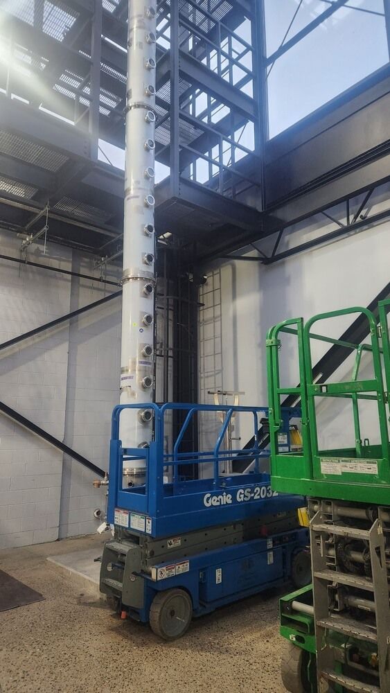 Blue scissor lift next to a tall, white and black structure inside a building.